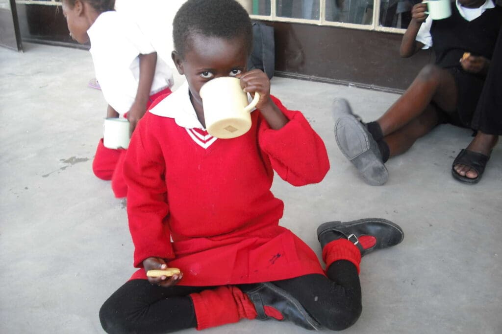 Little child in red school uniform drinking from a tin cup